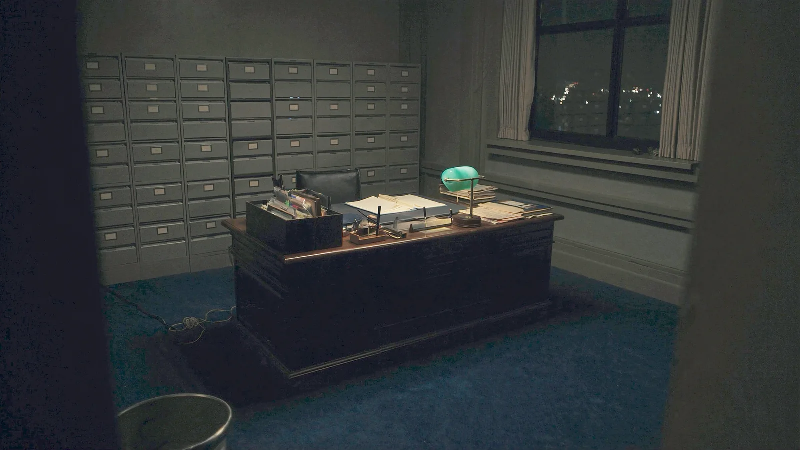 A dark private office at night with ledgers, document folders and a single desk lamp