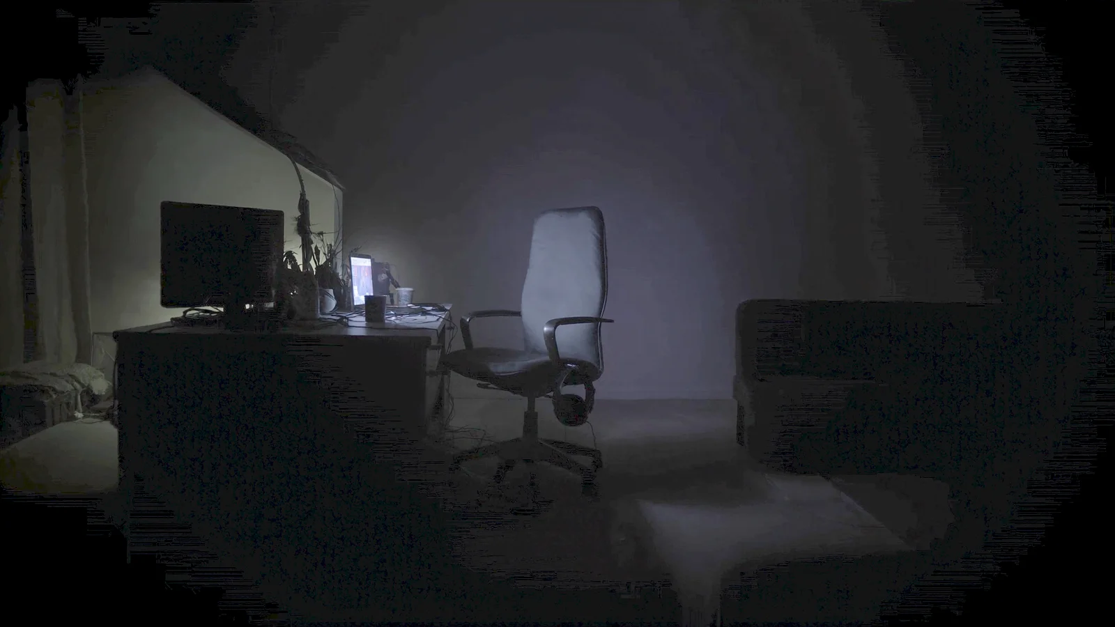 A laptop screen glowing in a dark empty room beside a gaming headset