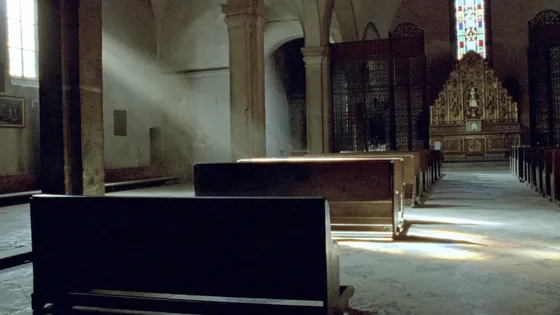 Light falling through stained glass across the empty pews of an old church